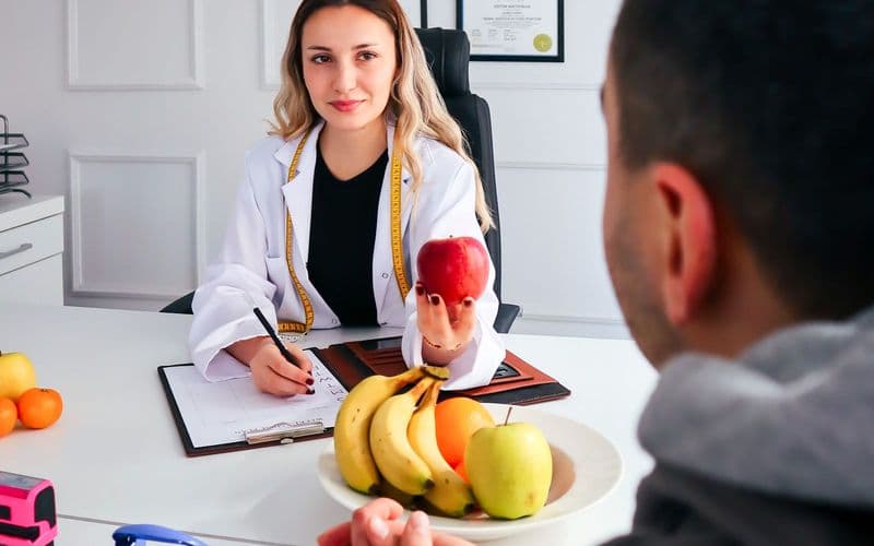 Une diététicienne reçoit un patient en consultation, une corbeille de fruits sur le bureau