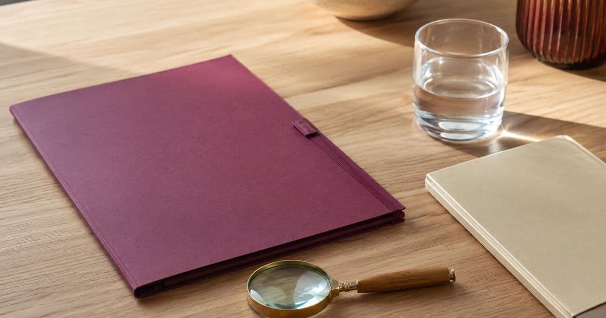 Chemise bordeaux, loupe et verre d’eau sur une table en bois clair