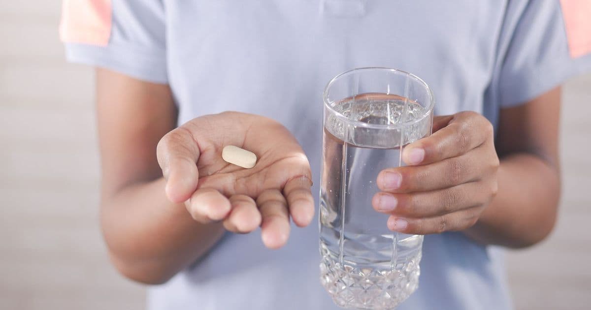 Une personne tient un comprimé et un verre d’eau