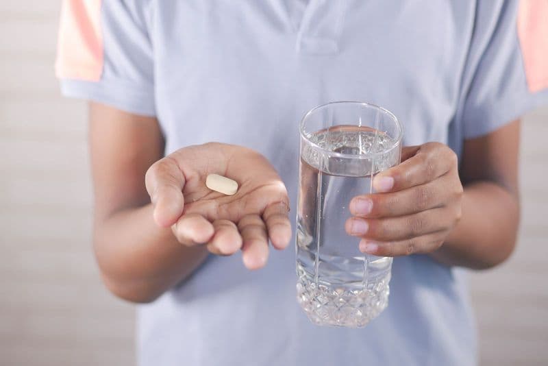 Une personne tient un comprimé et un verre d’eau